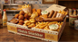 Dutch snack bar with a box of snacks and condiments on a wooden counter.